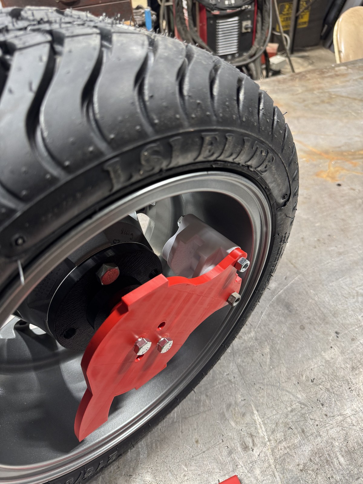 3D-printed red caliper bracket prototype mounted at the wheel for fitment verification before machining