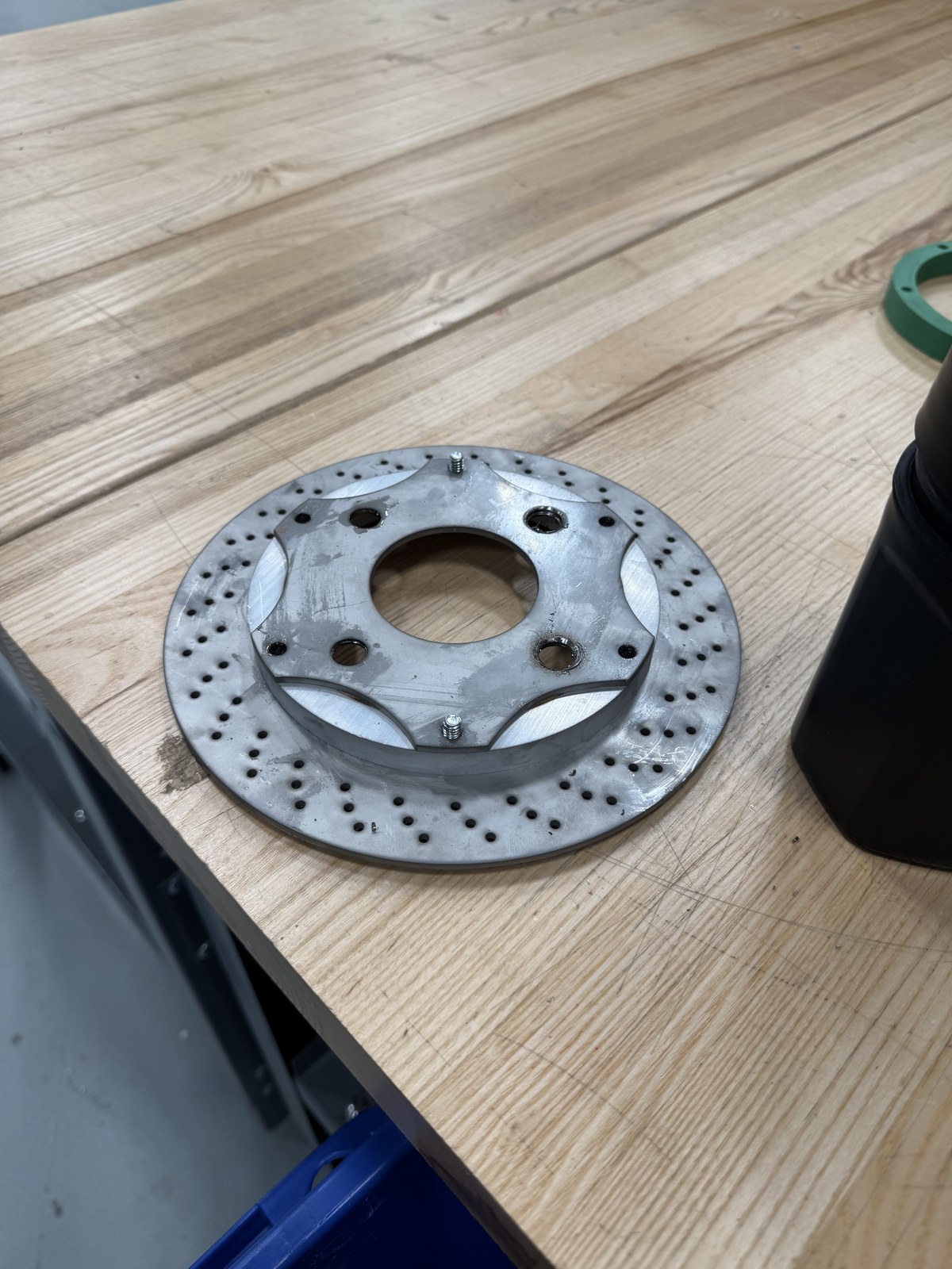 Custom two-piece brake rotor disassembled on workbench showing drilled outer ring and billet aluminum hub adapter