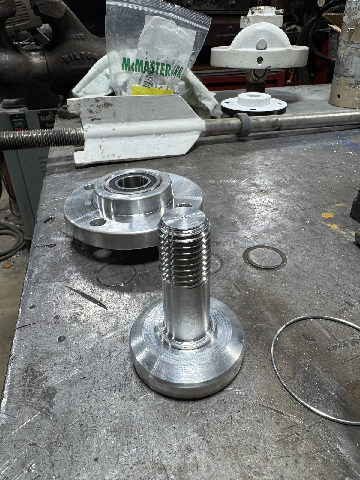 Finished custom-machined aluminum spindle on a workbench next to the matching hub and bearing assembly