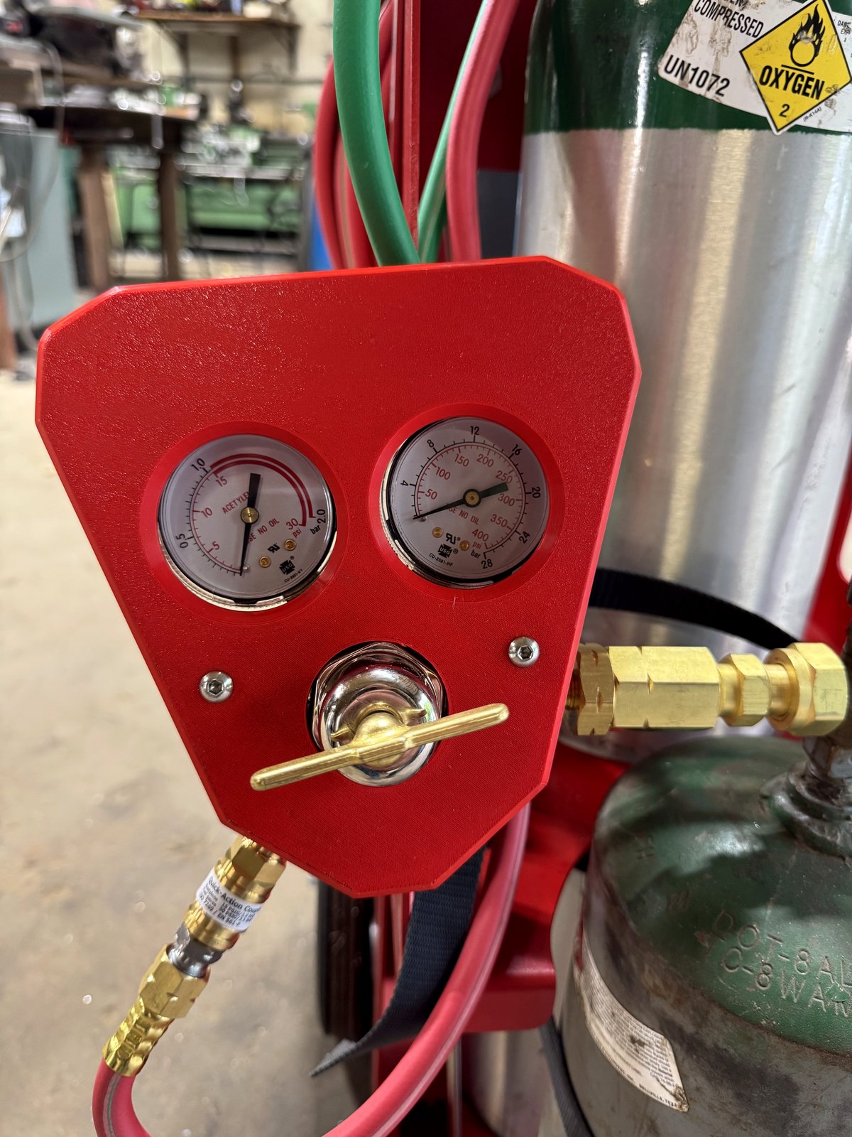 Close-up of red RegShield SM30 installed on an acetylene regulator, showing the gauge protection and brass T-handle access